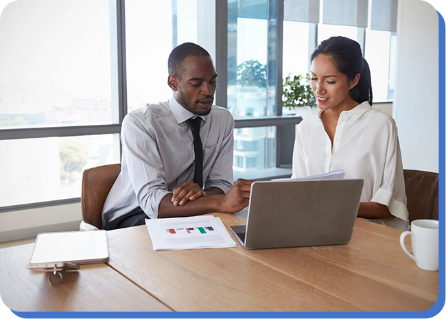 Two people sitting at a table looking at a laptop.